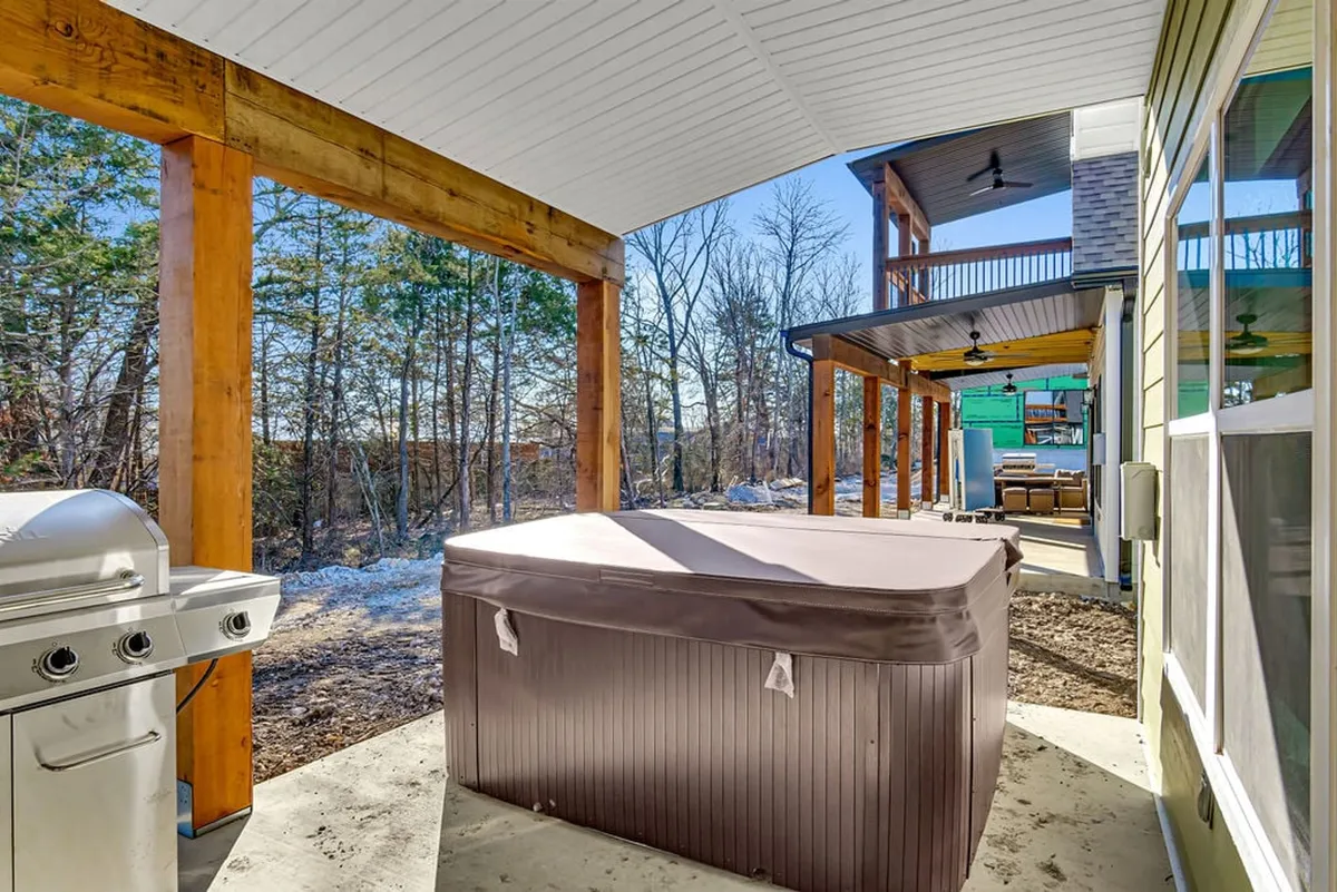This image captures a tranquil outdoor deck area featuring a bubbling hot tub, a grill, and sturdy wooden beams with natural surroundings in the background. The space invites relaxation and socialization, perfect for winding down after a day out or grilling dinner with friends.