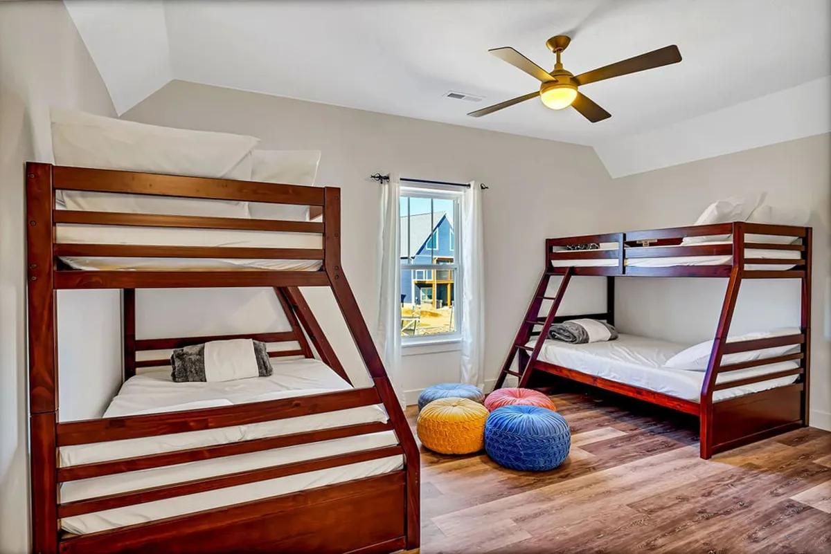A playful bunkroom with two sets of bunk beds, colorful poufs for additional seating, and a window offering natural light. The decor is cheerful, making the space inviting for children or families seeking a fun retreat.