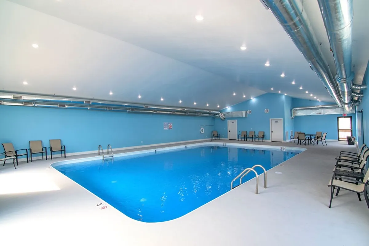 A bright and modern indoor swimming pool with inviting blue walls, lounge chairs along the side, and ample space for families to swim or relax. The tranquil atmosphere is perfect for year-round enjoyment, regardless of weather.