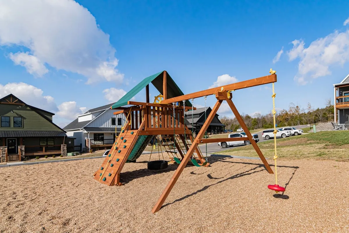 A cheerful playground with a swing set and modern climbing structures, surrounded by nearby homes. The area is designed for kids to play safely while families gather and enjoy the outdoors together.