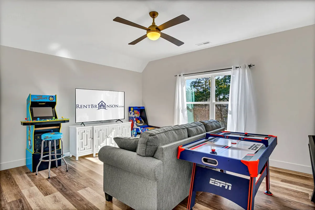 This image focuses on a classic arcade machine, an air hockey table, and a large TV, all arranged in a fun and relaxed setting. The elements are brightly lit and inviting, encouraging viewers to imagine themselves diving into hours of gameplay or a cozy movie night.
