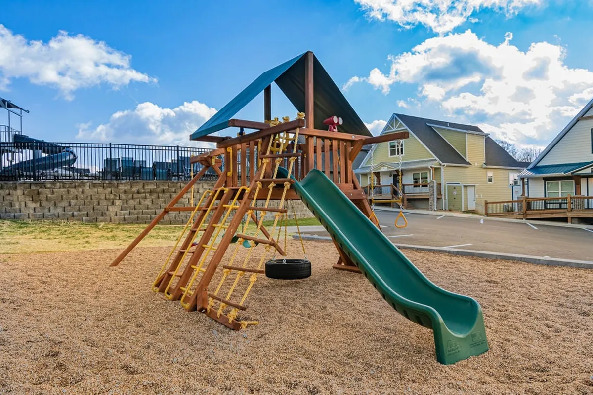 A well-equipped playground with slides and climbing structures, surrounded by green spaces. The scene is lively and welcoming, with room for children to play and families to gather for picnics.
